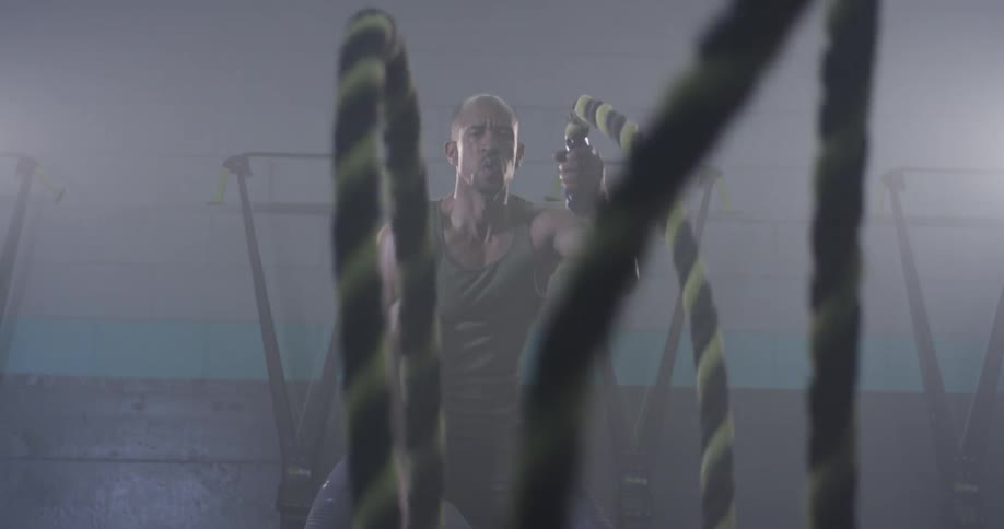 A muscular man whips two ropes up and down with one in each hand
