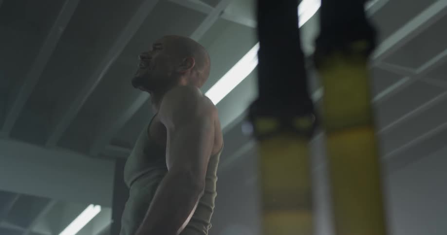 A man exercises in a gym with large ropes