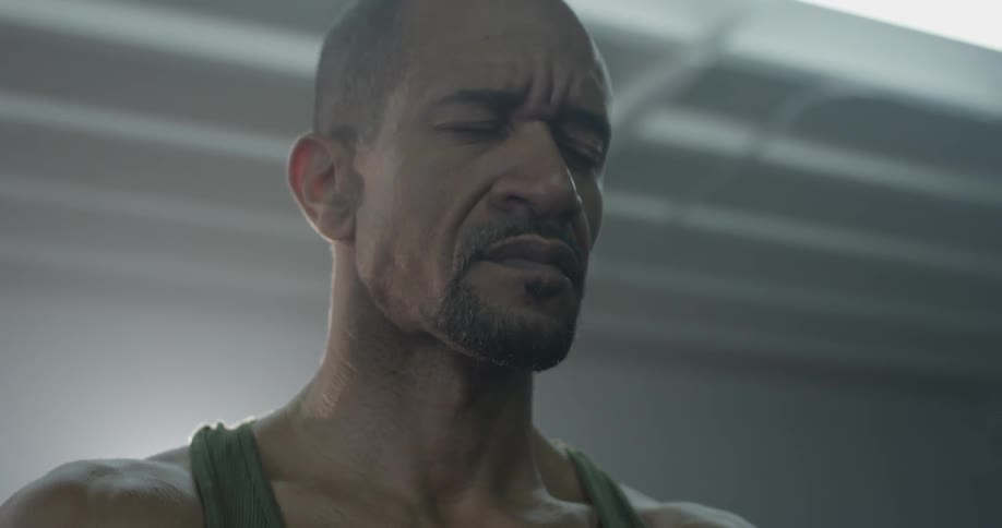 A muscular man stands in front of a bright light and breathes deeply