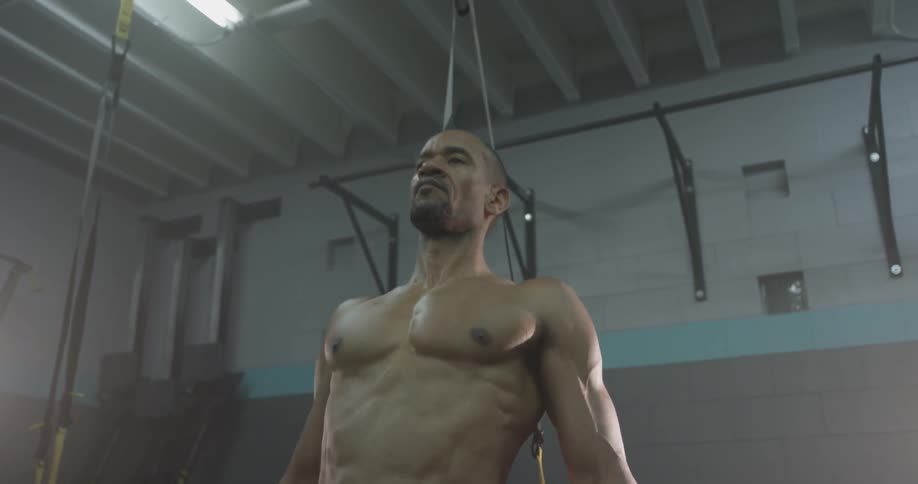 Shirtless mans stretches and warms up his muscles at a gym
