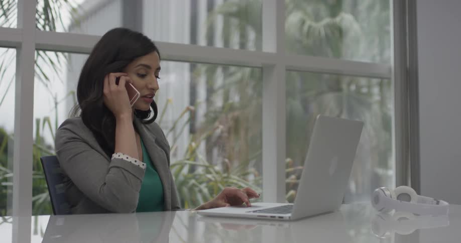 A woman typing info on a laptop and answering her phone
