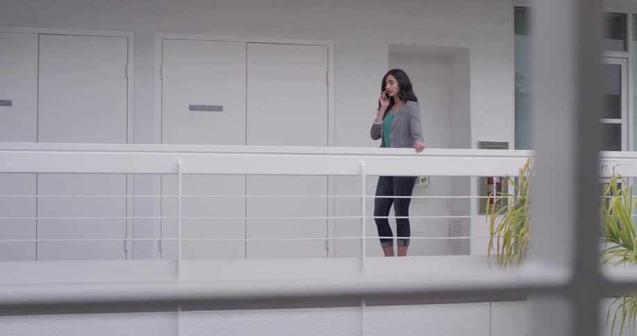 A woman talking on a phone while walking on a balcony
