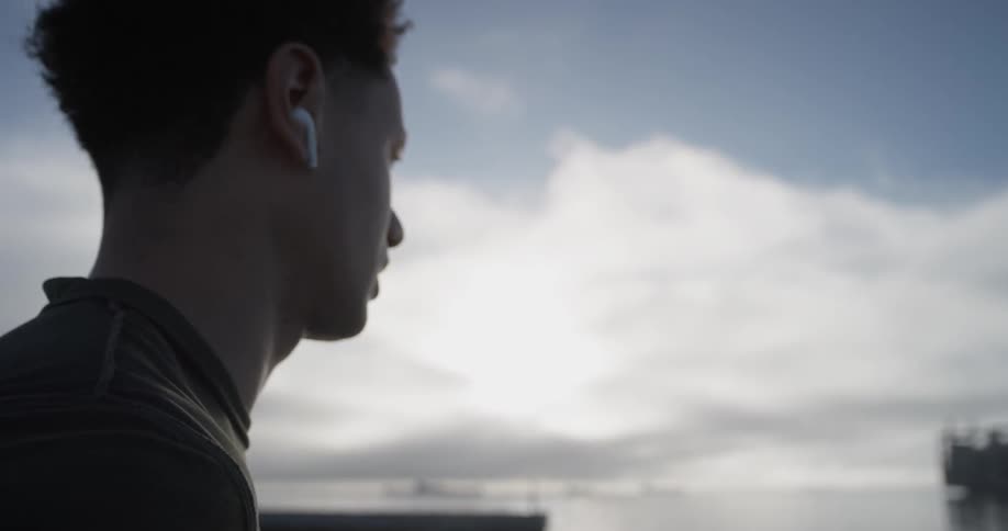Man walks with earbuds in ears near dusk