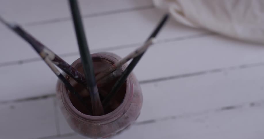 A person getting a paintbrush out of a jar of water