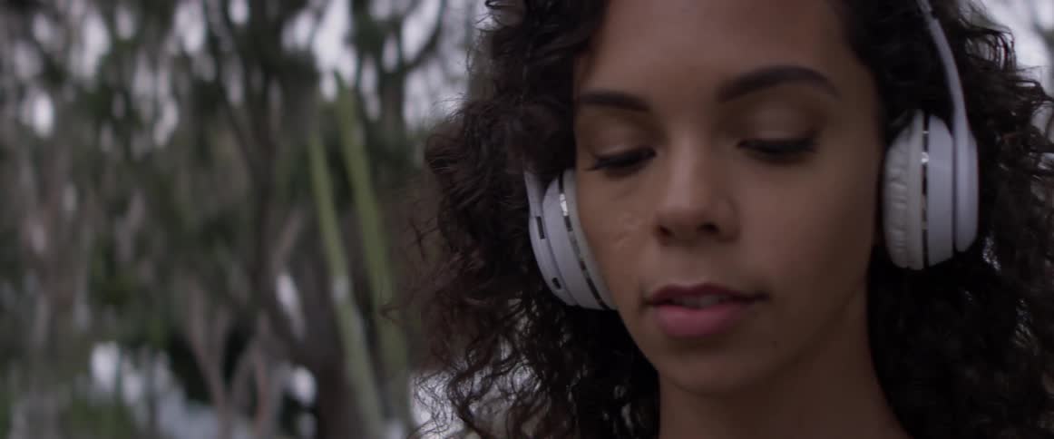 Woman wearing headphones stands outside by trees