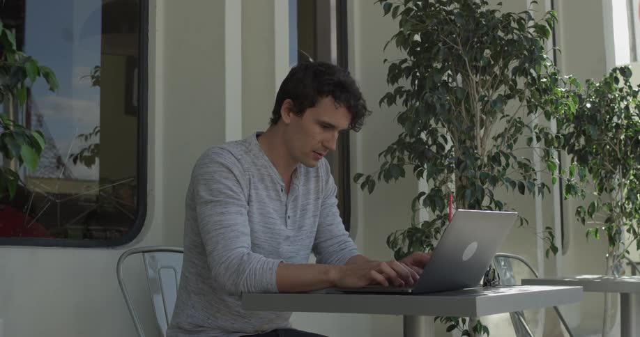 Man types on computer while sitting outside at table