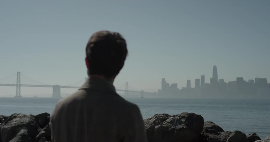 Man near rocks starts out a bridge in distance