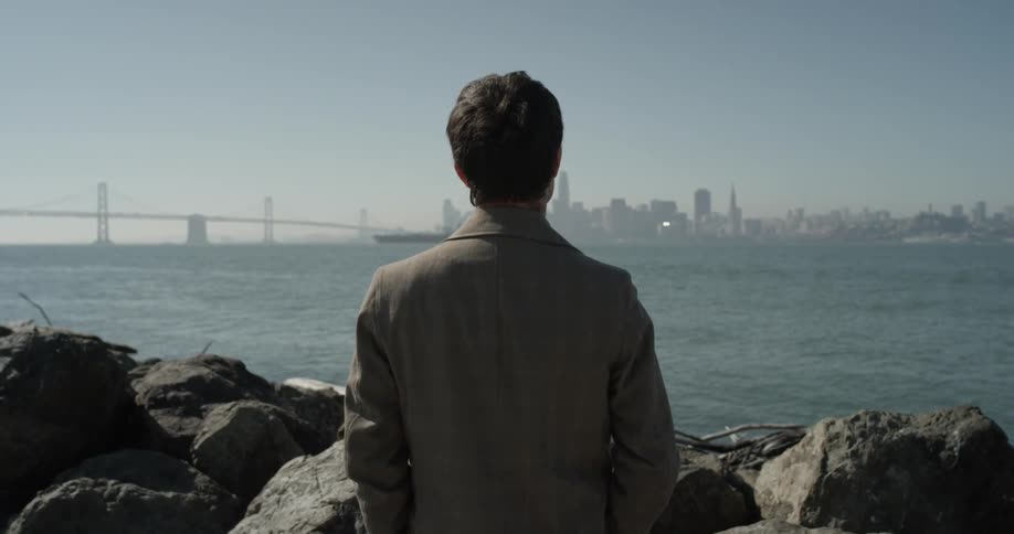 Man stares across water to city in background