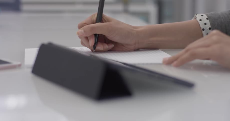 A woman using a tablet and writing things down on paper