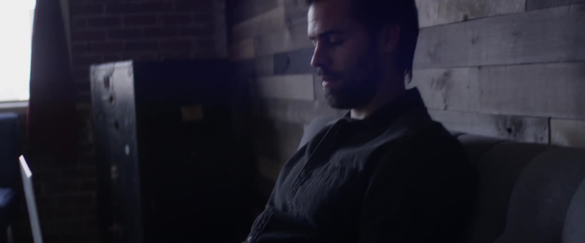 A man sits on a sofa typing on a laptop on his lap