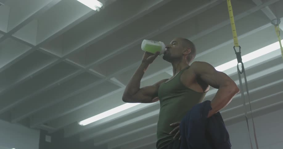 Man in tank top opens water bottle a drinks green liquid