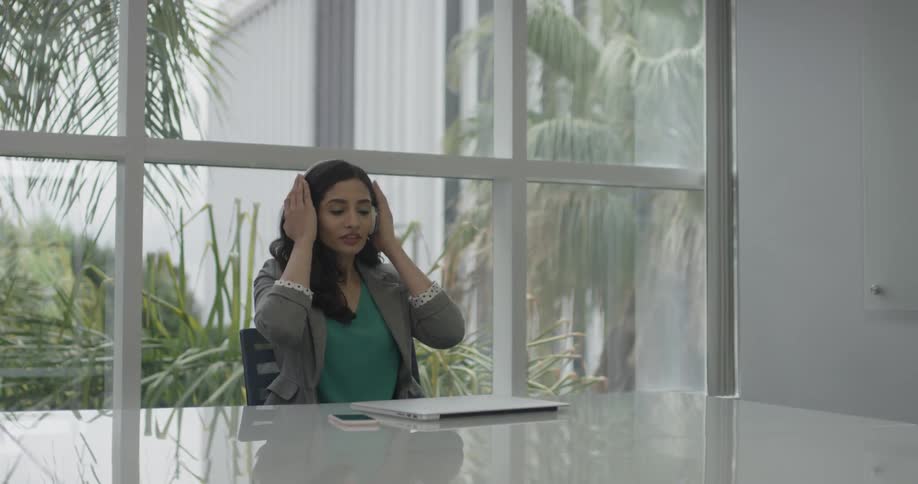 A woman sitting at a desk closes her laptop and puts on wireless headphones