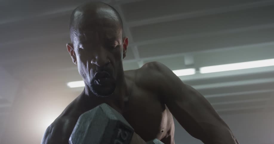 A muscular man lifts weights as he sits
