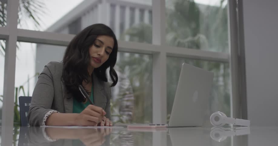 A woman writing on a paper and looking at a laptop