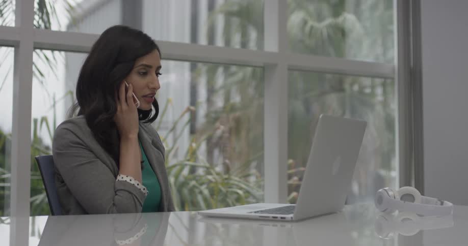 Woman talks on a phone looking at her laptop