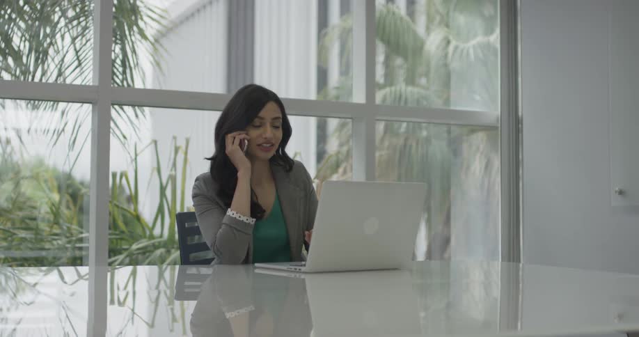 Woman answers the phone while working on a laptop in an office