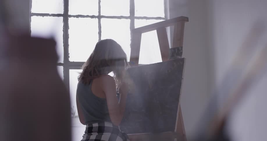 Woman holds an easel and paints on canvas
