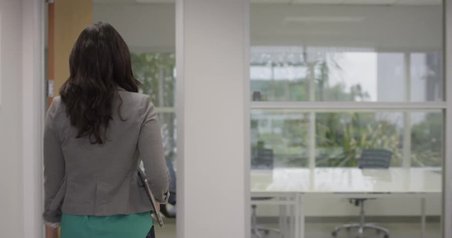 A woman walks into an office with a laptop