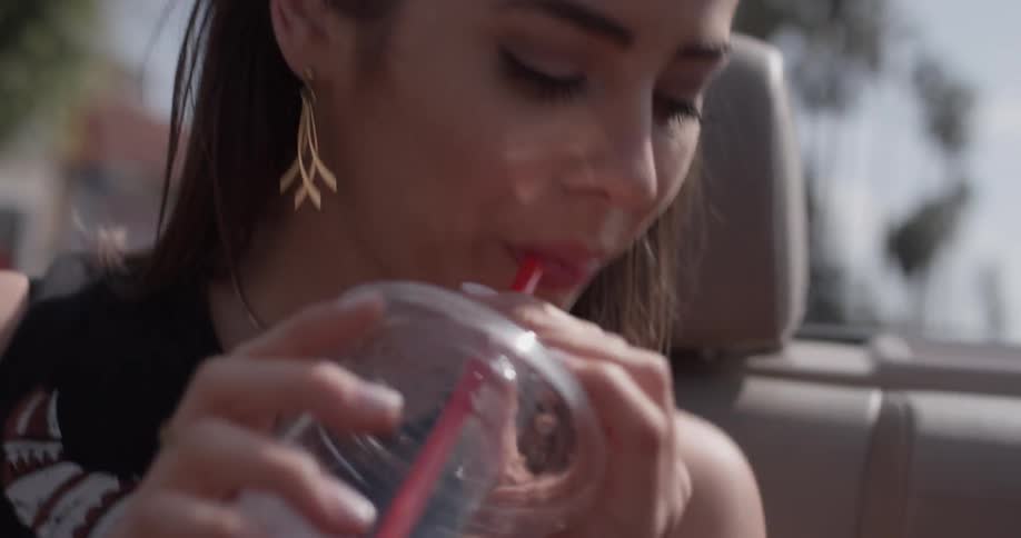 Woman sips from a cup while riding in a convertible