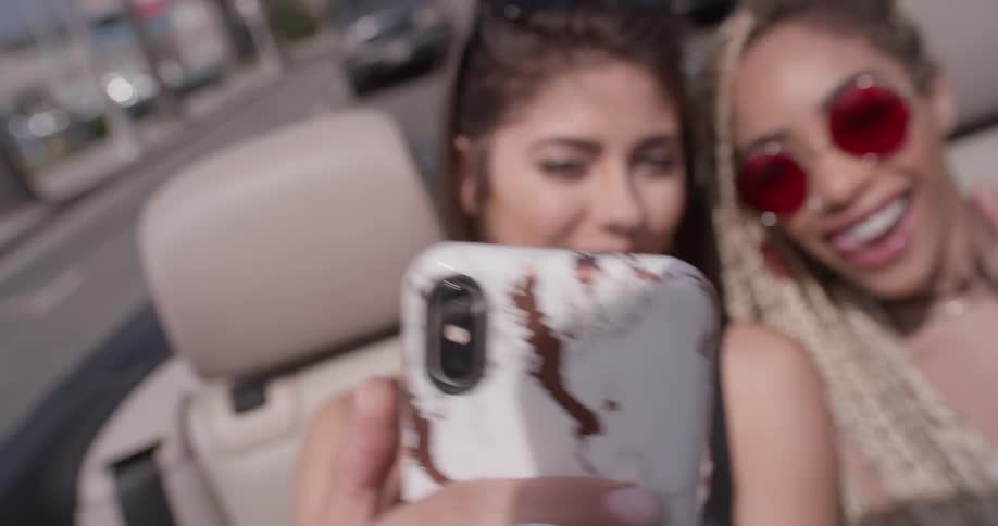 Two women in the backseat of a car pose for a selfie