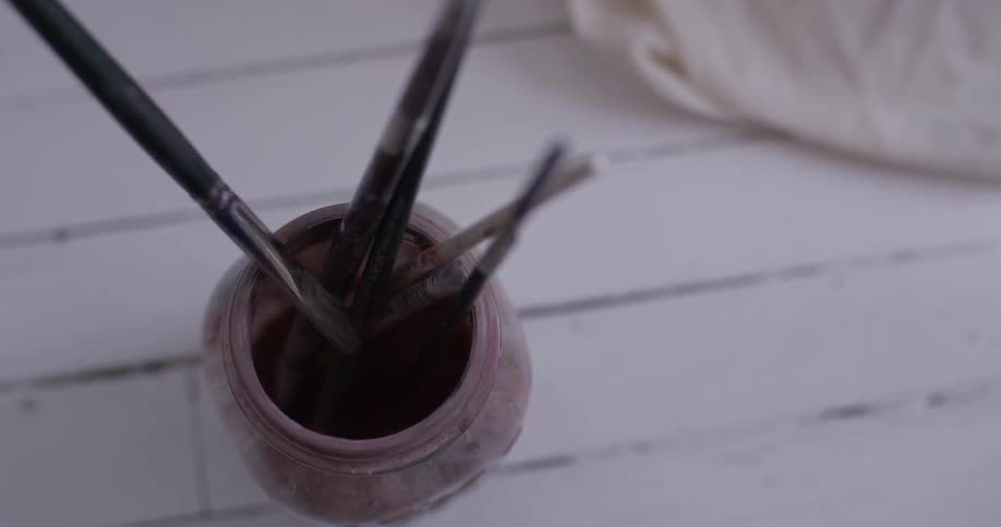 Hand picks up paintbrush out of jar with several paintbrushes