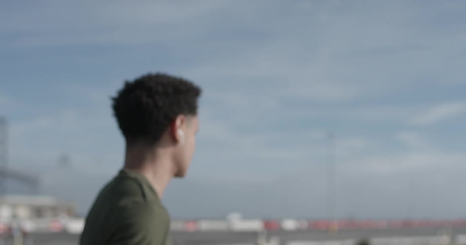 Man with earbuds looking out towards sky while camera moves away