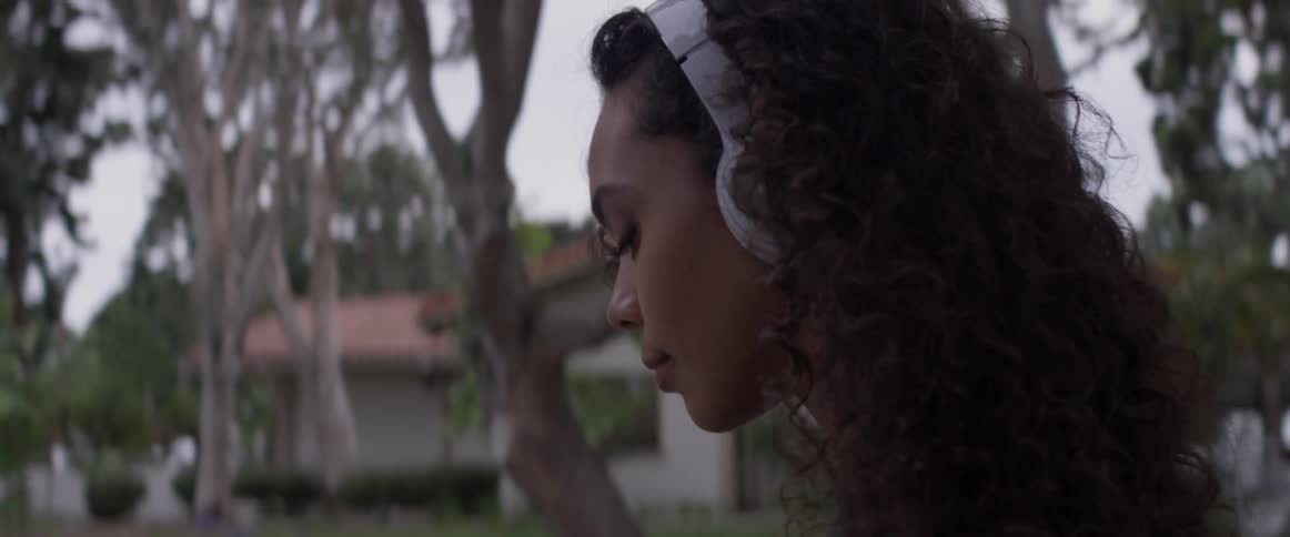 Woman wearing headphones stands outside by trees
