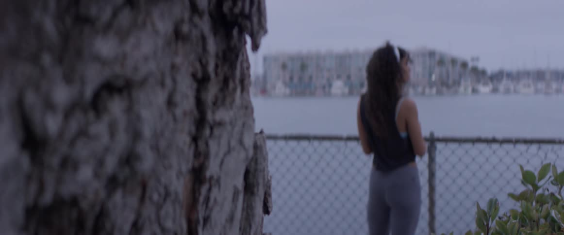 Woman stands at chain link fencing looking out at the water