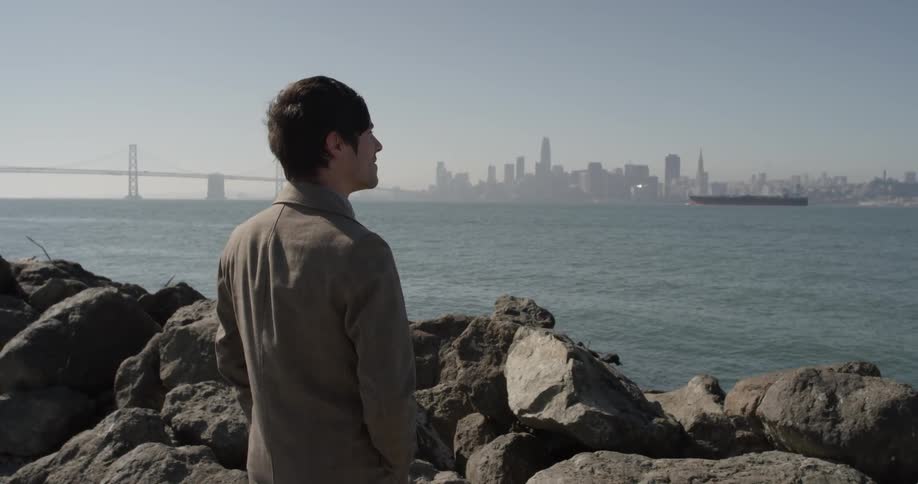 A man standing at some rocks looking over a city