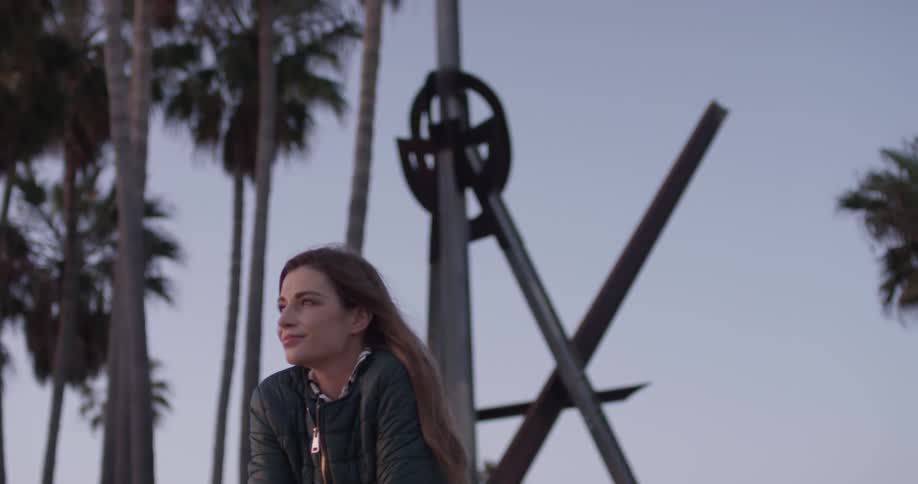 Woman sits outside by palm trees on a cloudy day