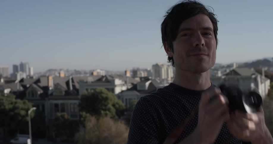 A man holds up a camera and looks through the lens