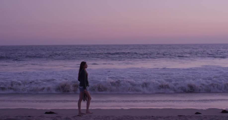 Woman walking in front of the ocean at sunset