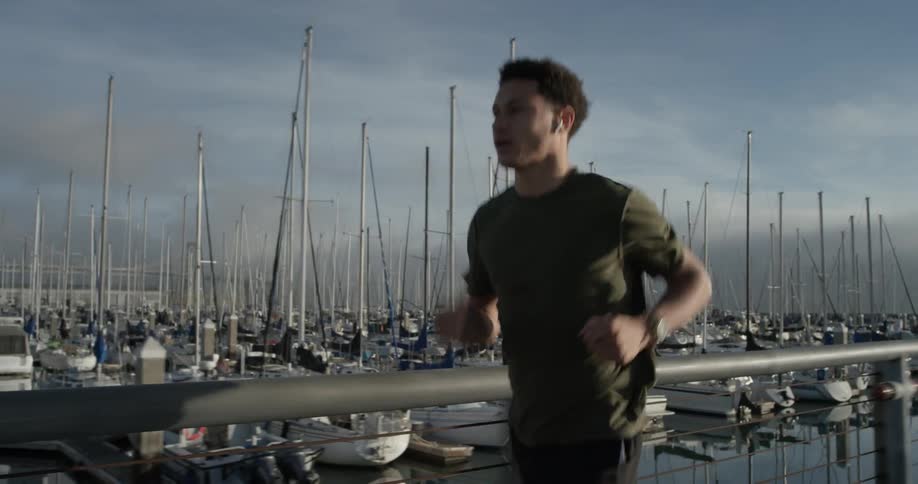 Man jogs across bridge with boat marina in background