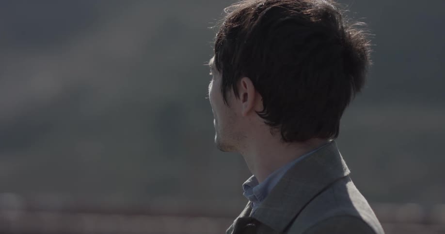 Man looks down at something while cars pass in the background