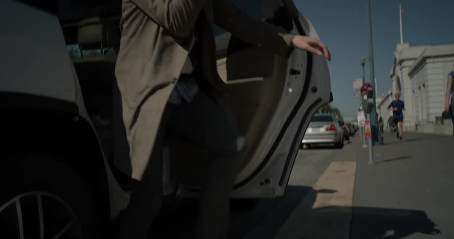 A man steps out of the back seat of a car onto the sidewalk of a bright blue sunny cloudless day