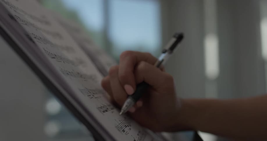 Person's hand writes on a sheet music