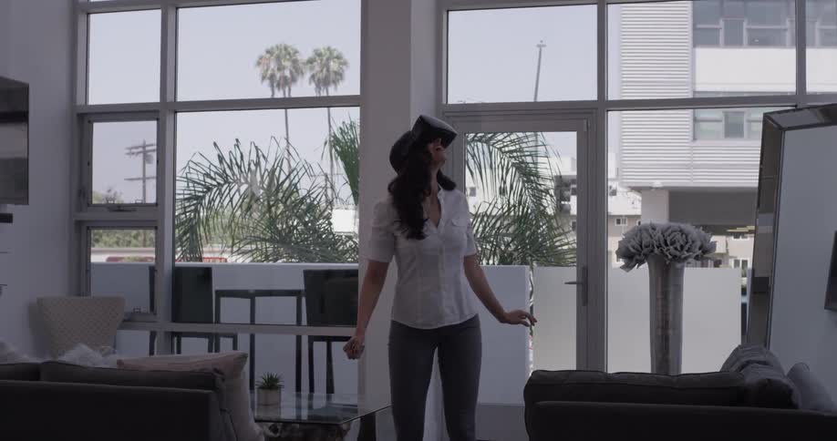 A woman stands in a brightly lit house wearing a vr headset