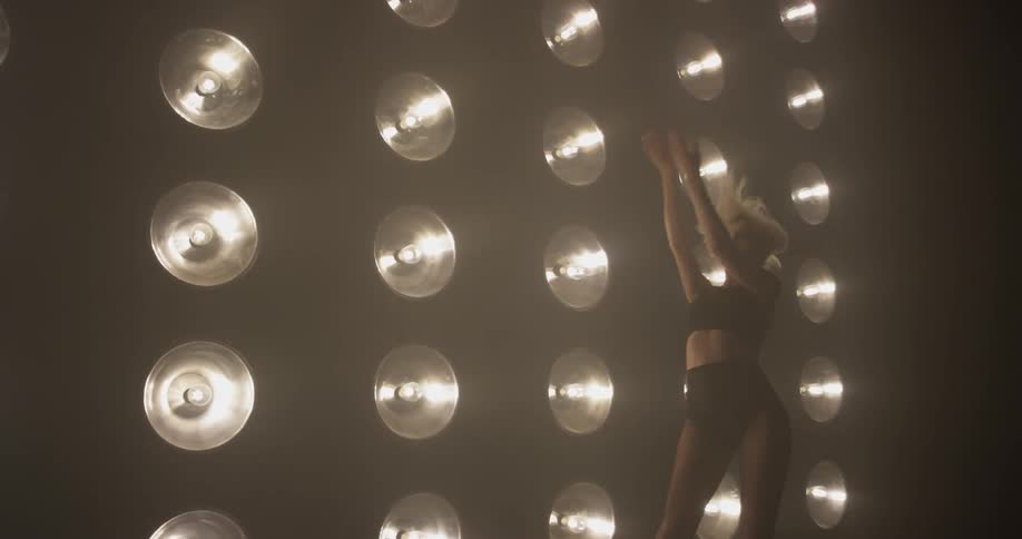 A woman is dancing in front of multiple large lights
