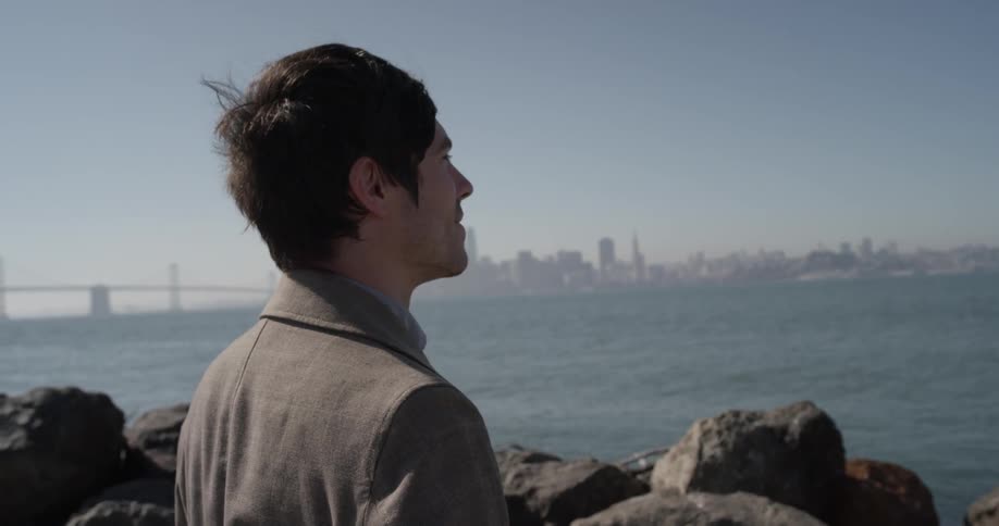 A man standing on the rocks across from a city