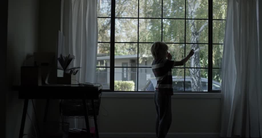 Boy at window stares at something in his hands