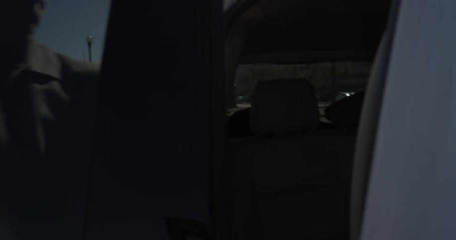 A man is approaching a vehicle to open a door and get in outside in daylight