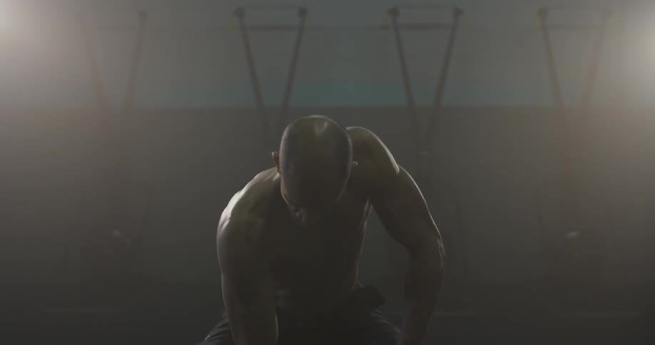 Shirtless man sits on a weight bench and curls dumbbells