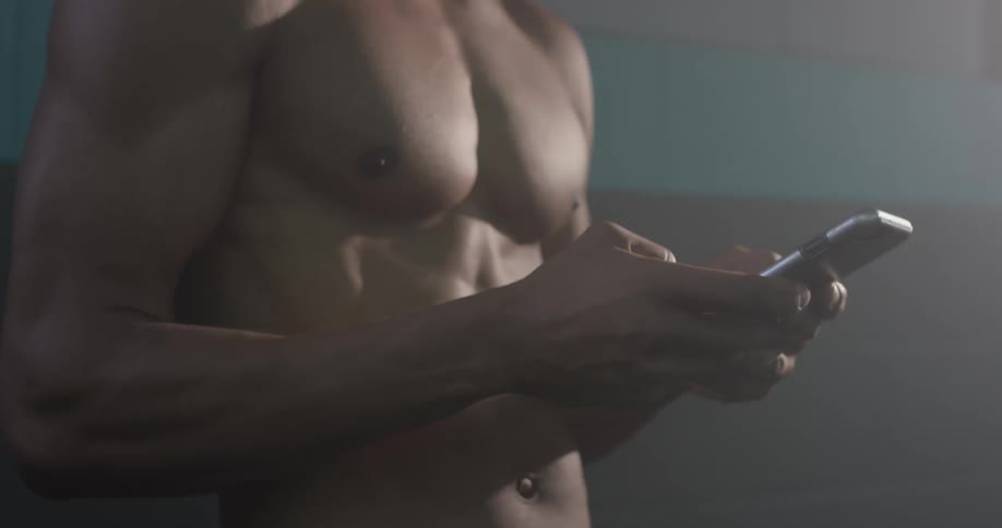 A shirtless man types on his cellphone
