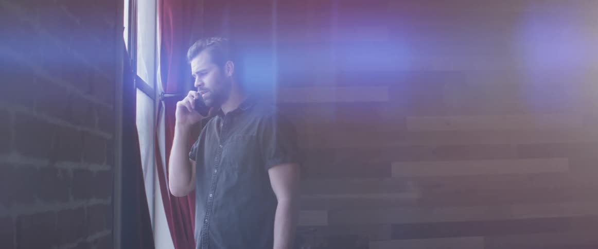 A man talking on a phone looking out a window