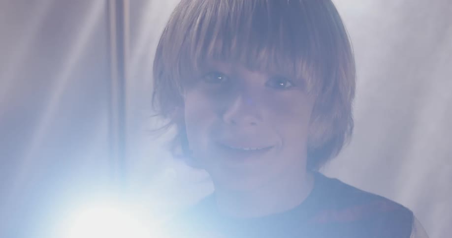 A boy shines the light of a flashlight into the camera inside his tent