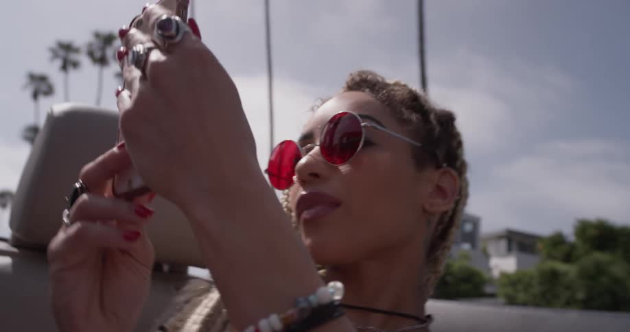 A woman takes a selfie in the back seat of a convertible