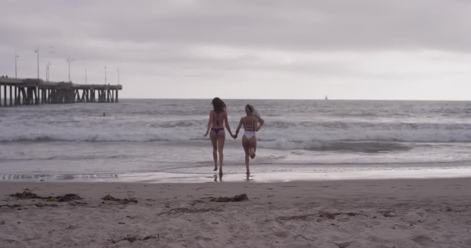Two women in bikinis running into the ocean