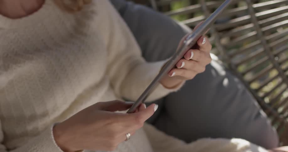 A woman touches a tablet as she sits in a wicker chair