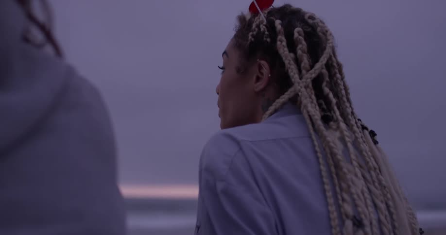 Women can be seen sitting down on a dark cloudy night at the ocean beach looking out at the horizon and discussing things