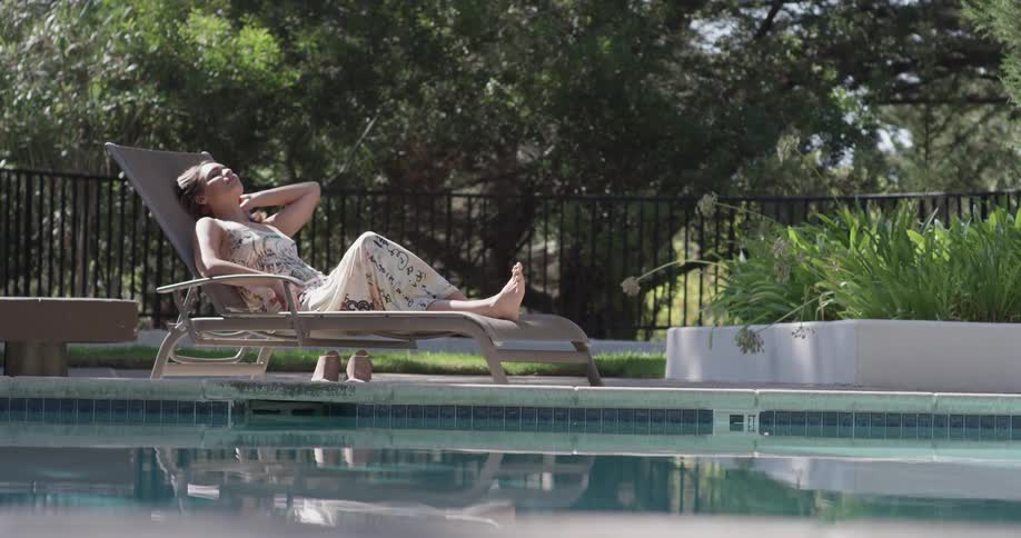 A woman sits in a dress by a pool